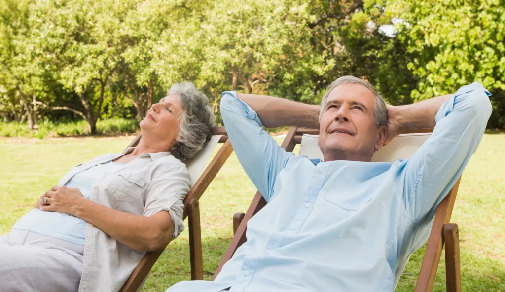 Un couple de personnes âgées se détendant sur des chaises longues dans un jardin verdoyant.