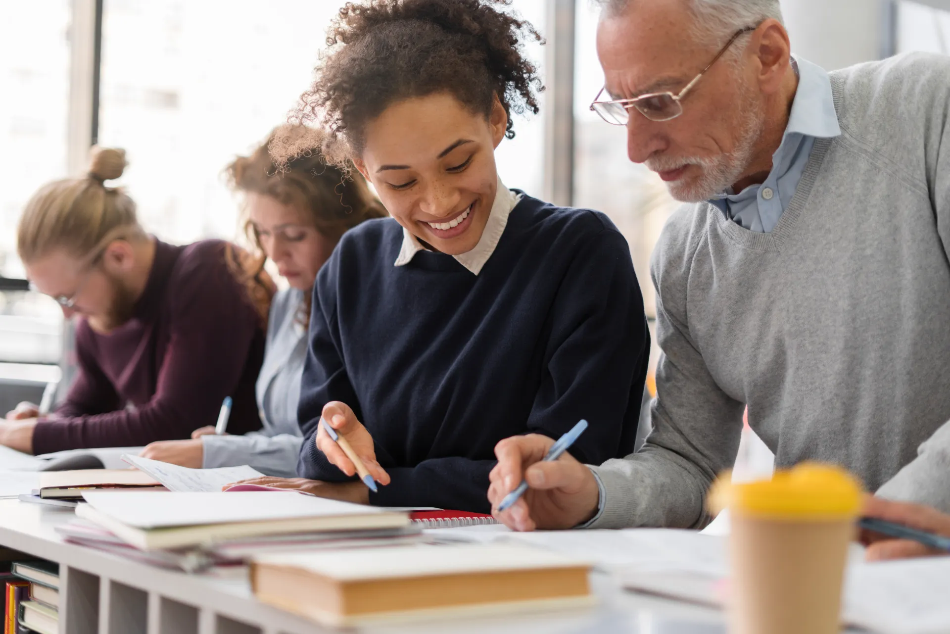 Un groupe d'étudiants est assis à une table, concentré sur leurs travaux, certains écrivent et d'autres consultent des livres.